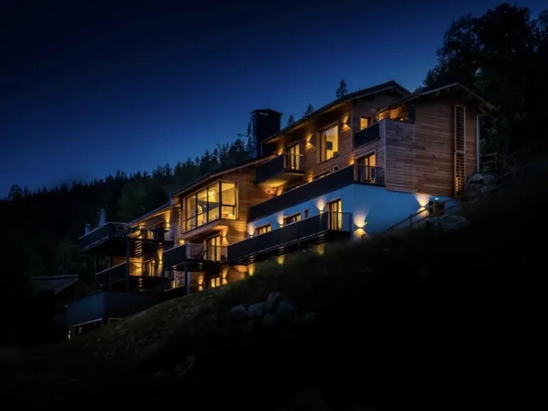 Le Chalet Mont-Blanc lit from within at dusk, set into the forested southern slope above the Chamonix valley