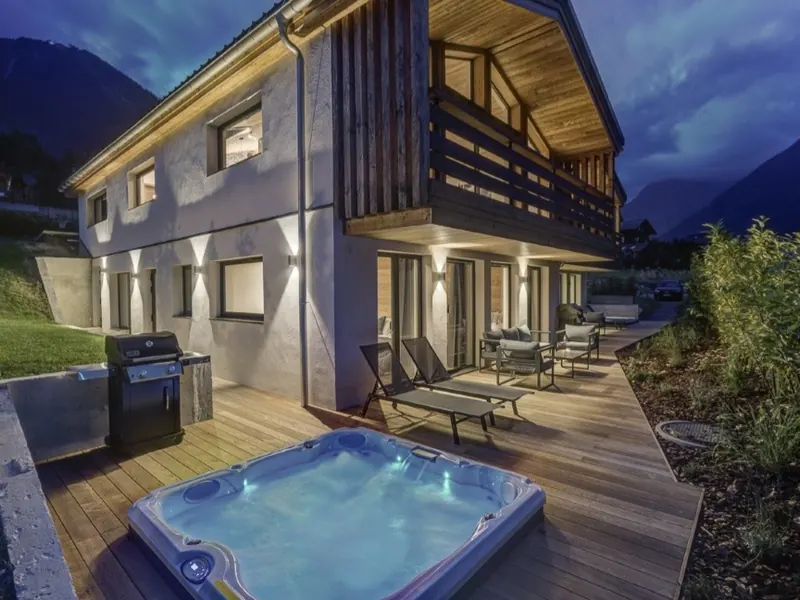 Chalet Chouca at blue hour, its terrace hot tub glowing beside the timber facade, Chamonix