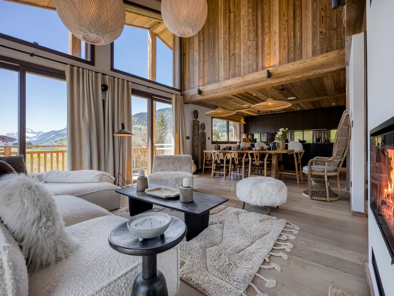 The living room at Chalet Gypset, a fire lit beside tall windows onto the snow, Megève