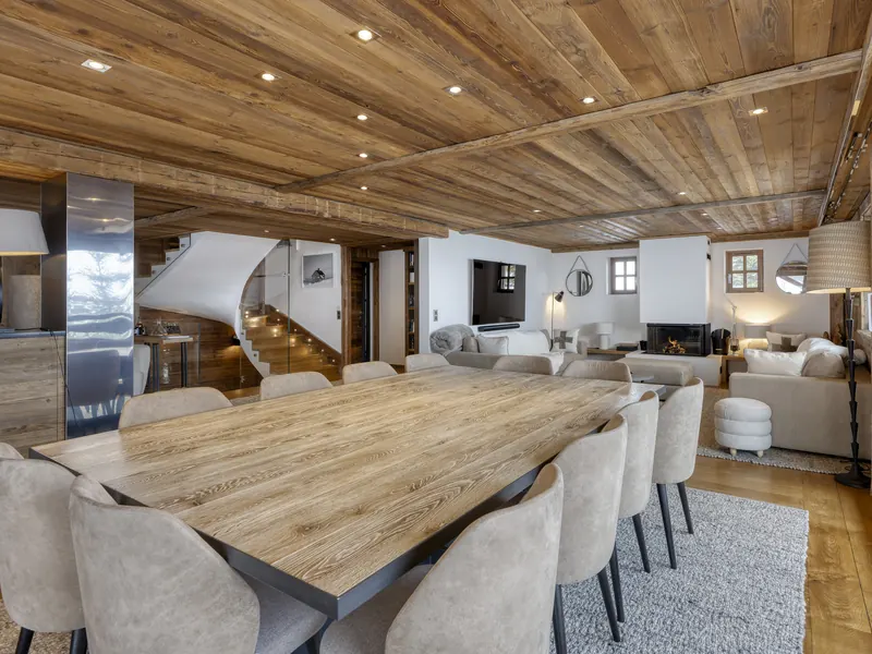 The dining table and open kitchen at Chalet Les Hauts de Megève, pale oak under a timber ceiling