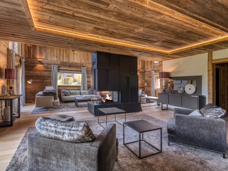 The living room at Chalet Ours Blanc, a long fire burning under a warm-lit timber ceiling, Megève