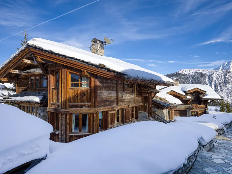 Chalet SJ under deep snow against a clear blue sky, the Courchevel slopes rising behind