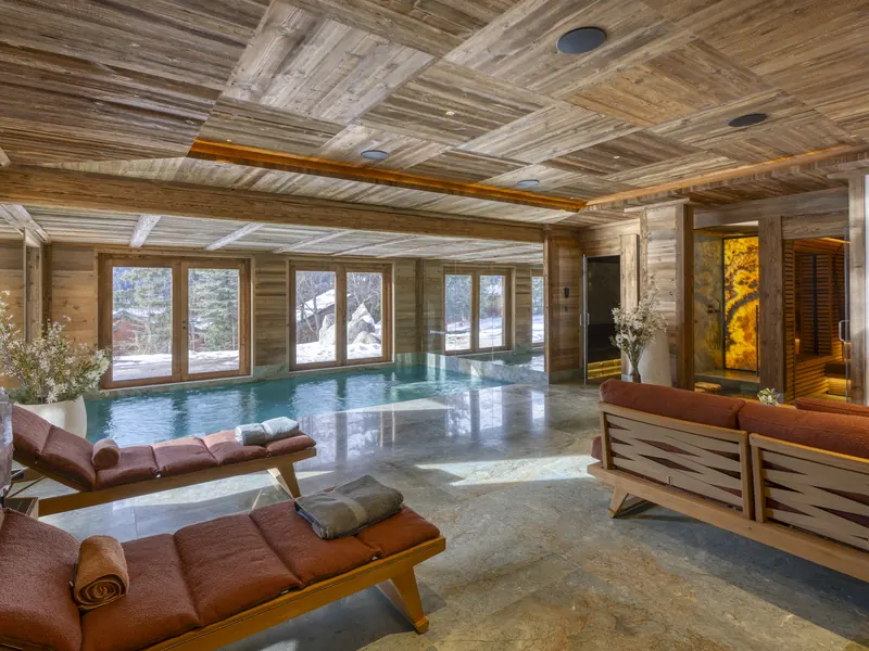 The pool room at Chalet Crystal, a long lounger beside still water under warm timber, Méribel