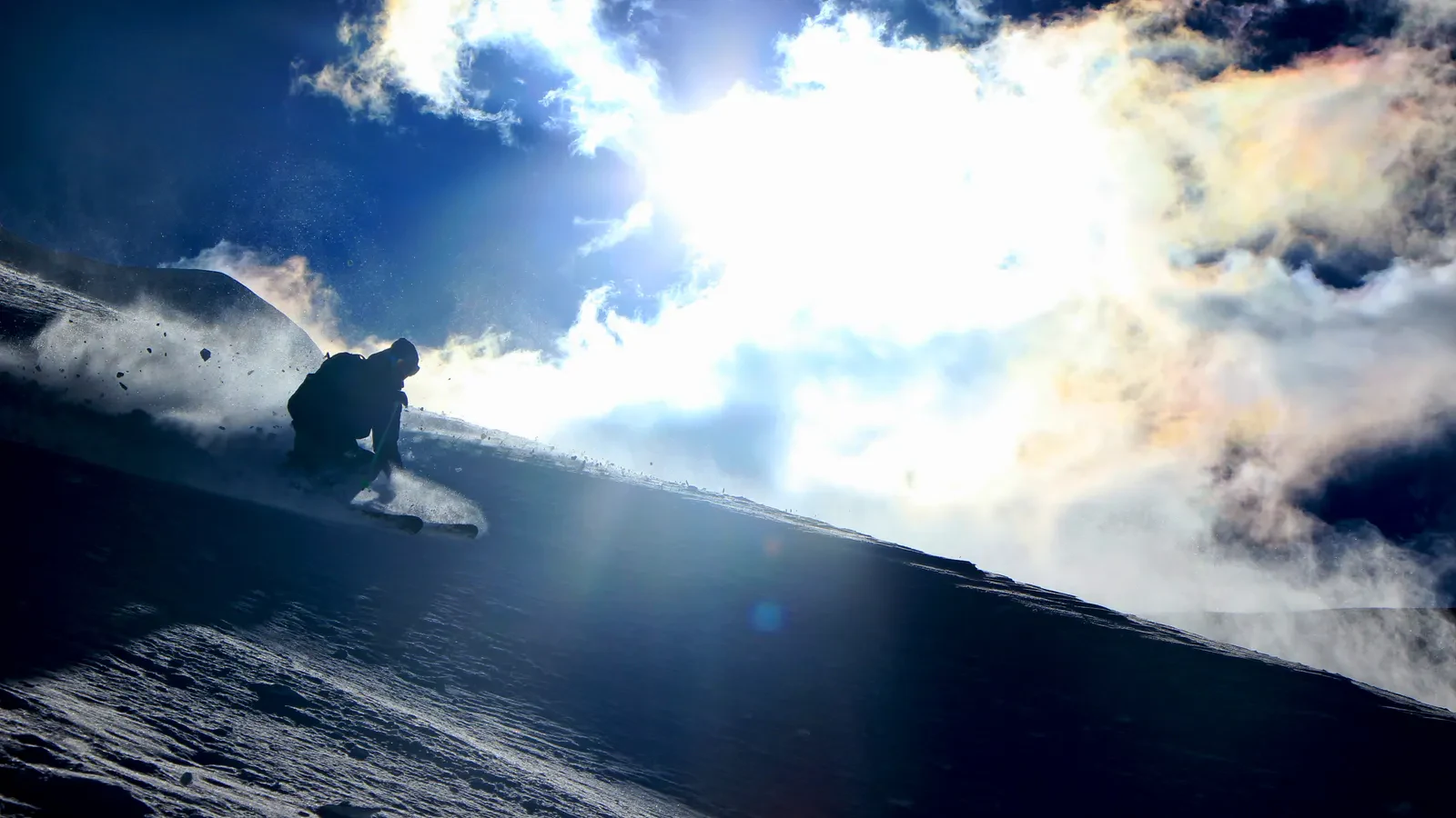 A skier backlit by the sun, throwing up a plume of powder